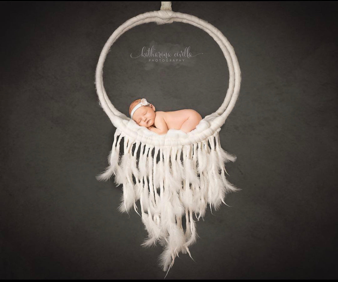Newborn photography dream catcher prop fully wrapped in wool with felted hanging strands and marabou feather details, shown in use during a newborn photo session.