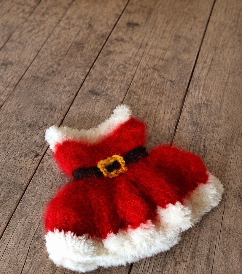 A small red and white fuzzy dress with a black belt and gold buckle detail, photographed on a rustic wooden surface.
