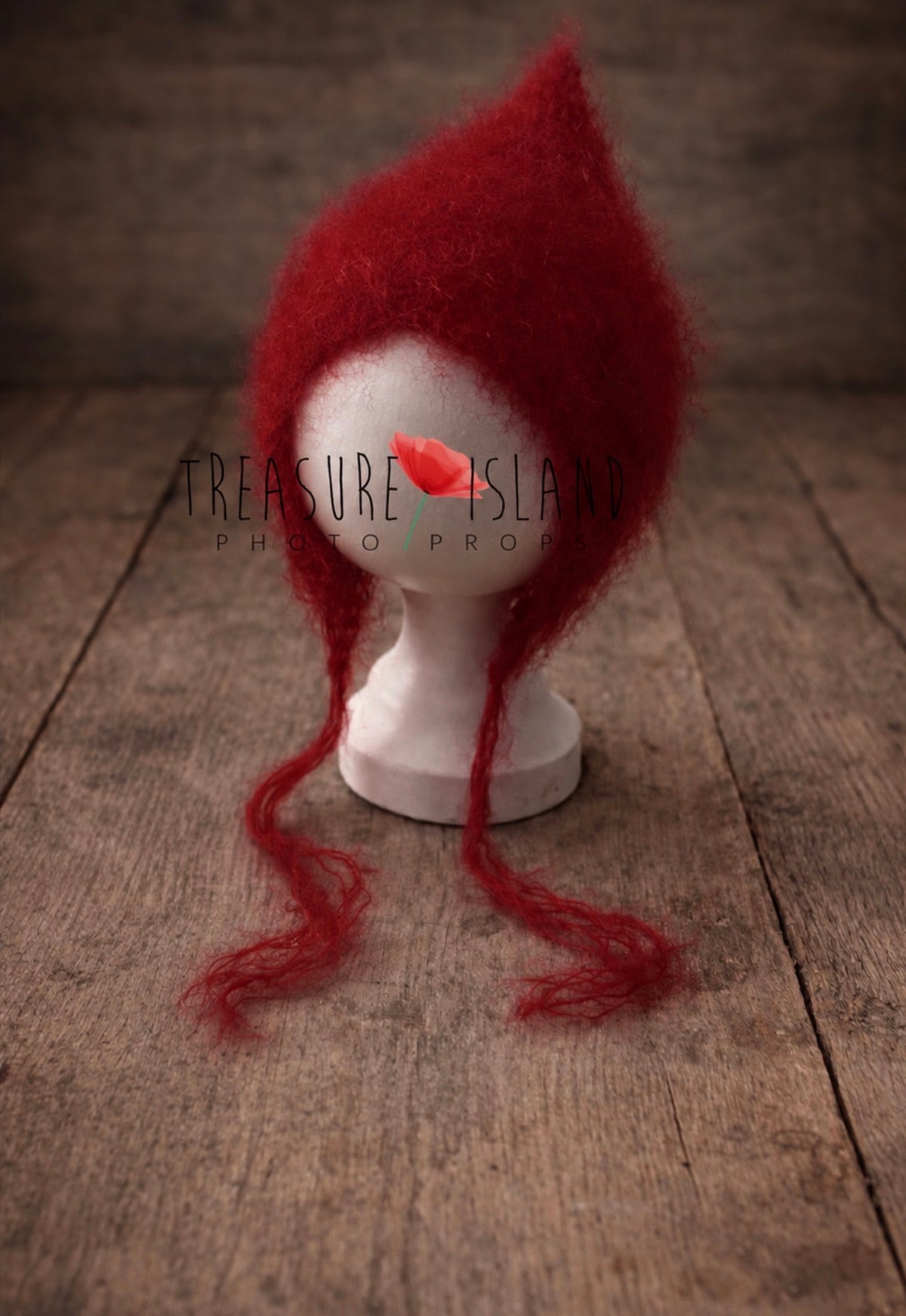 Handmade red newborn pixie bonnet made of soft mohair, displayed on a white mannequin head on a rustic wooden floor background.