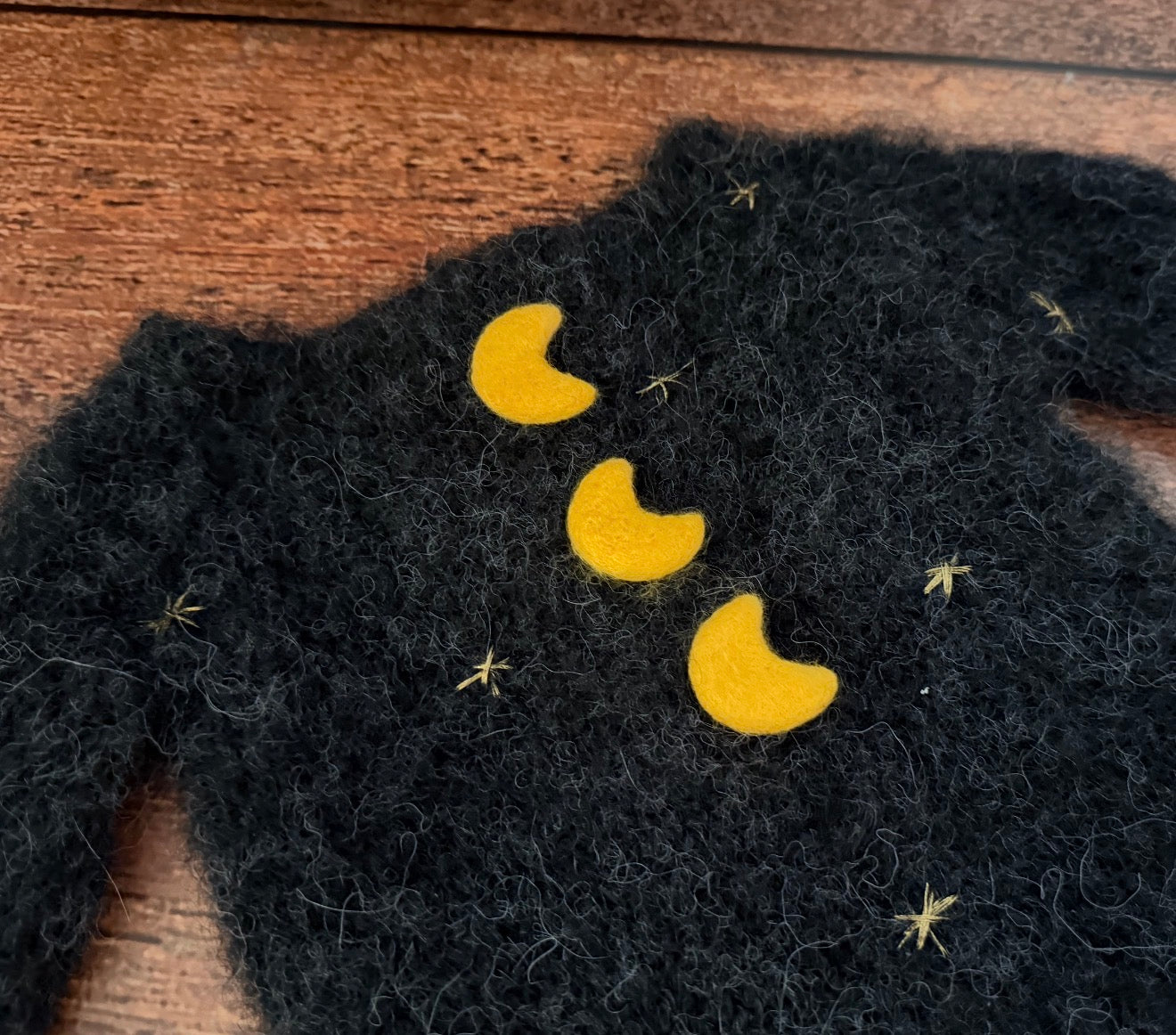 Close-up of black witch knitted romper with hand-felted golden moons and embroidered stars for Halloween photography