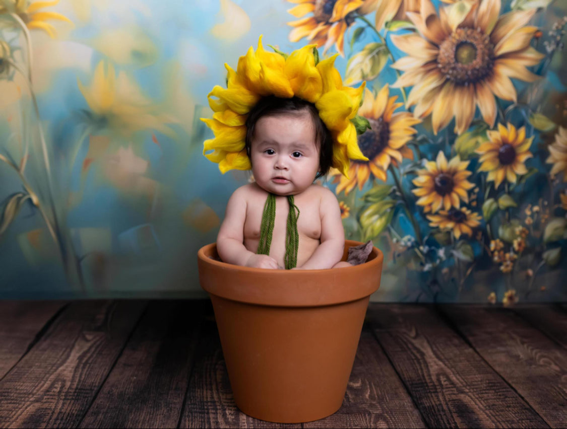 Newborn wearing a felted sunflower bonnet in a floral photography setup