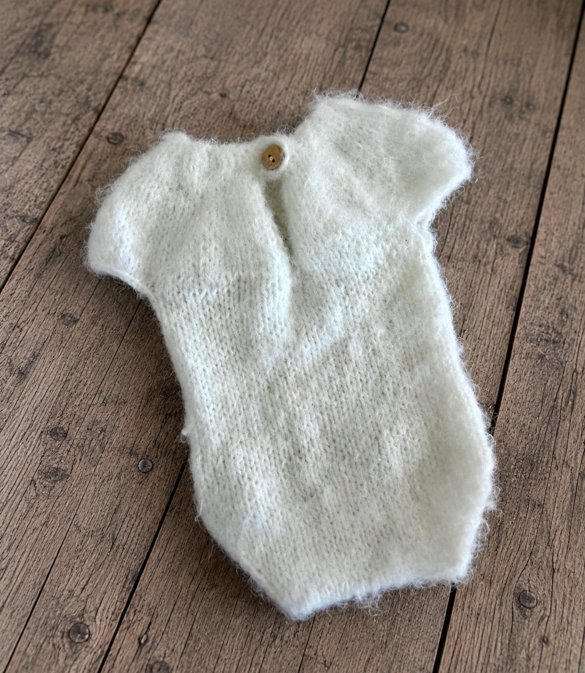 Handmade ivory fluffy knitted photography bodysuit showing its back opening and single-button fastening on rustic wooden flooring.