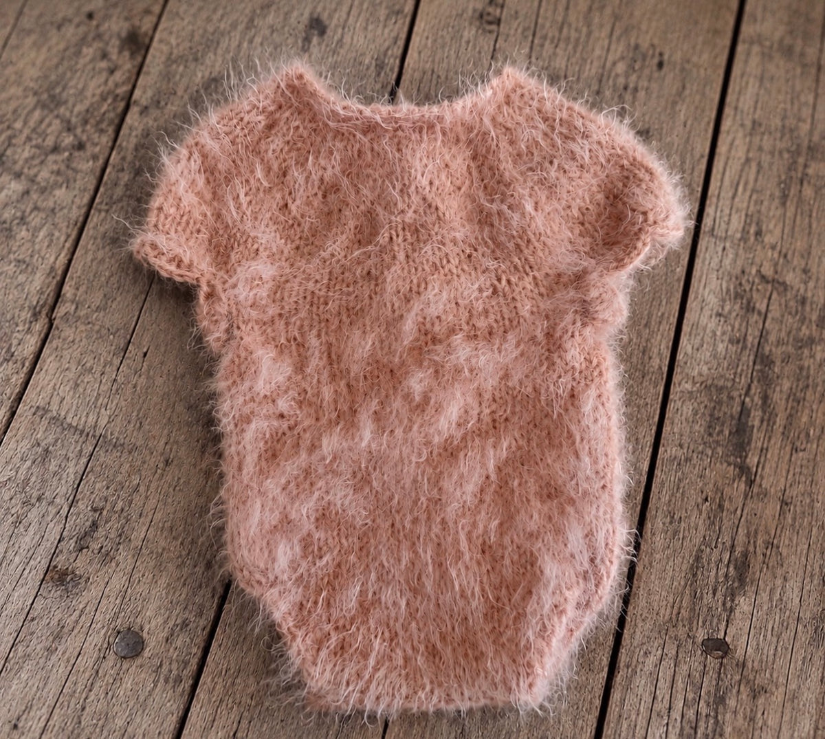 Dusty pink short-sleeved fluffy knitted bodysuit with decorative edges, photographed on a rustic wooden floor.