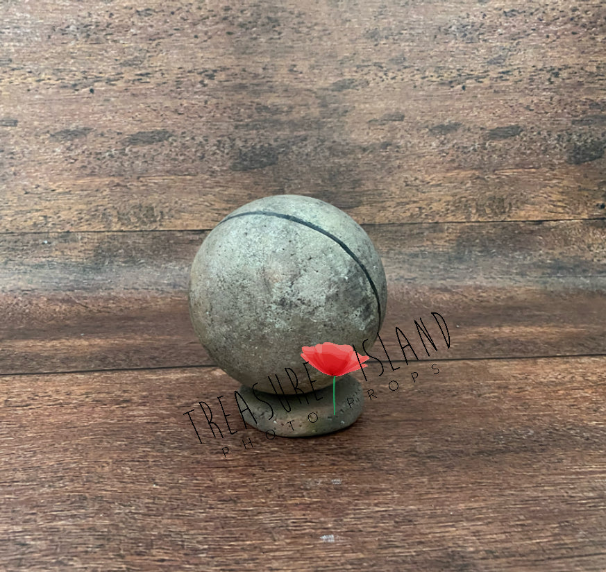 Handmade styrofoam globe photography prop with a textured grey-green finish, dark curved line and round base, displayed against a rustic wooden background
