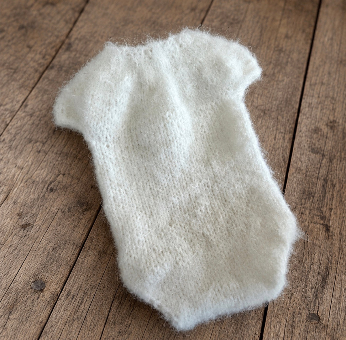 Front view of an ivory fluffy knitted short-sleeved bodysuit for newborn and sitter photography, displayed on a rustic wooden floor.