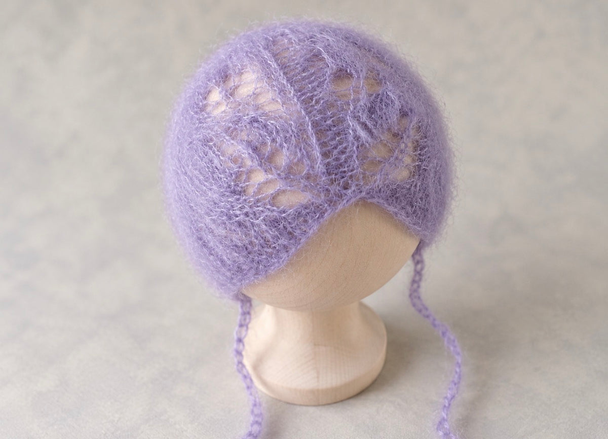 Close-up of lavender hand-knitted mohair bonnet with delicate openwork pattern and long ties