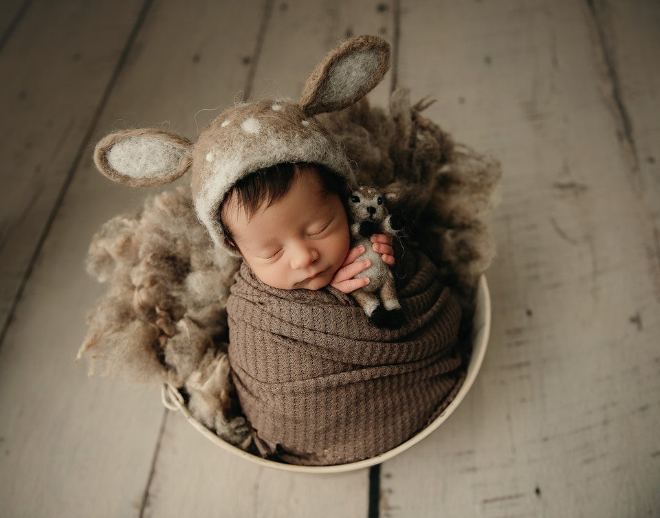 Newborn wearing a hand-felted deer bonnet with matching miniature deer toy in a neutral woodland photography setup