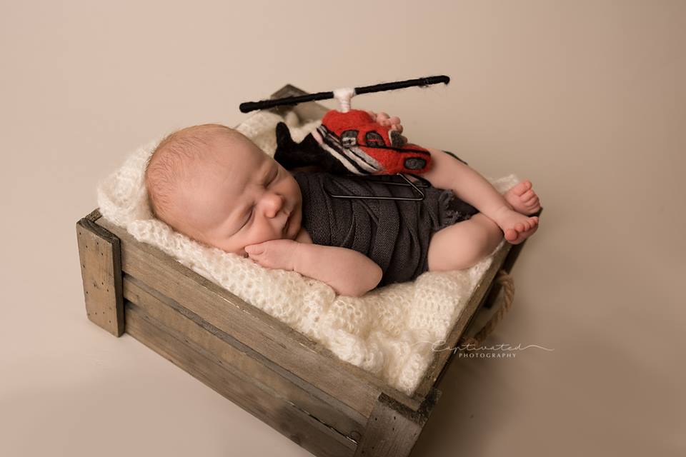 Newborn photographed with hand-felted rescue helicopter in aviation-themed setup