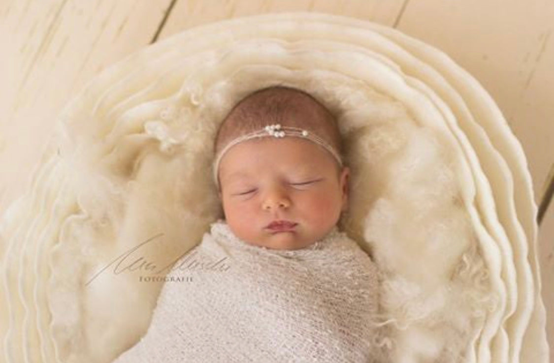 Pearl White curly wool blanket used as a soft textured layer in a newborn basket setup